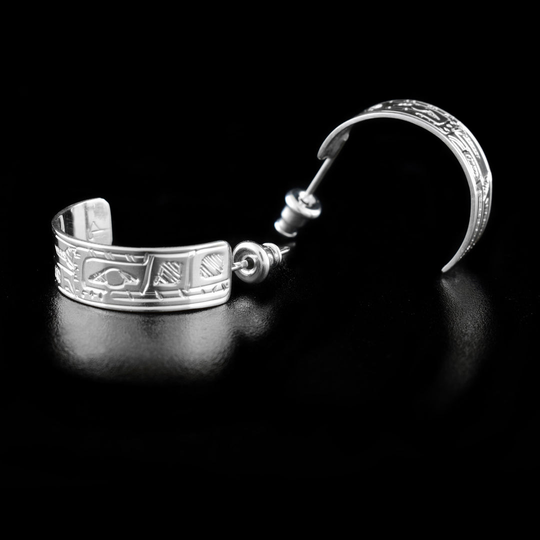 These stud hoop earrings are made from sterling silver and have wide bands curved into a hoop with a gap in the back. There are depictions of the Wolf carved into the surface of the band.