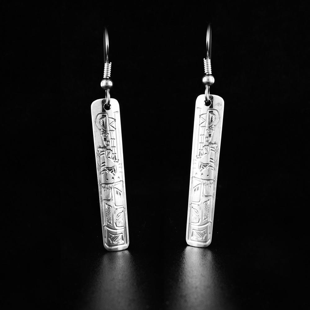 These dangling wolf earrings are made from sterling silver and have thin, rectangular hangs. There are depictions of the Wolf carved into the surface of the hangs.