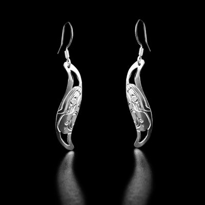 Sterling Silver Leaf Style Eagle Earrings by Harold Alfred. Each earring is in the shape of a leaf. The artist has hand-carved the profile of an eagle's head facing downwards in the center of each earring. The eagle has a short, large beak pointing downward. It also has a feather on the top of its head. The background is cut out.