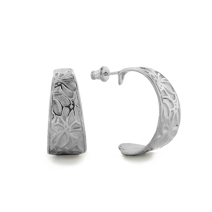 These flower hoop earrings are made from sterling silver and have wide, curved bands with a gap in the back. There are textured patterns of flowers on the surface of the hoops.