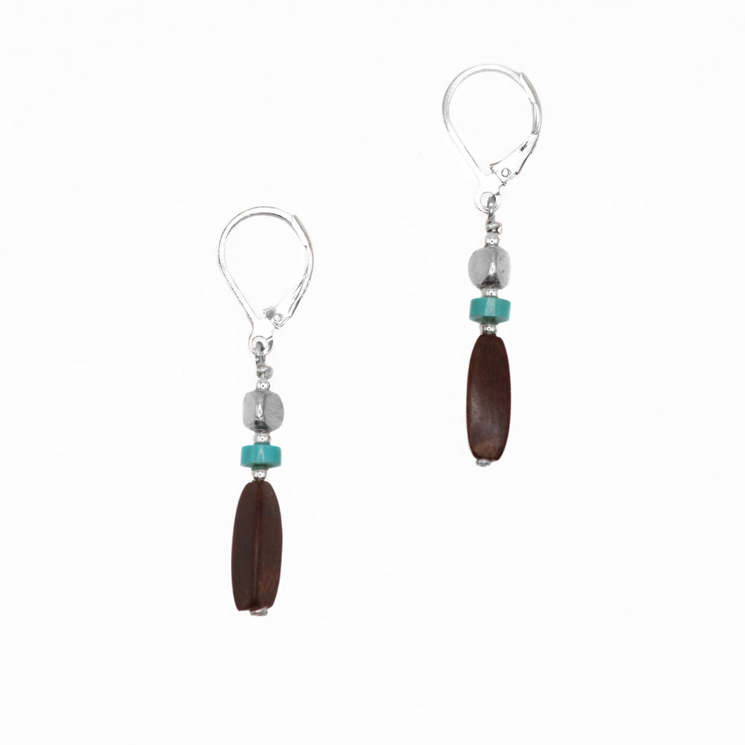 These ebony stone and turquoise drop earrings have cube, silver charms, flat round turquoise bead and a long cylinder ebony at the bottom. The hangs dangle from the hooks.