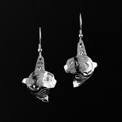 Silver Mini Orca Earrings by Fred Myra. Each earring is in the shape of an orca with the tail right underneath the orca's head. The artist has hand-carved intricate designs along the orca's body to represents the unique black and white spots as well as the fins. The artist has attached the bail to the orca's dorsal (top) fin.