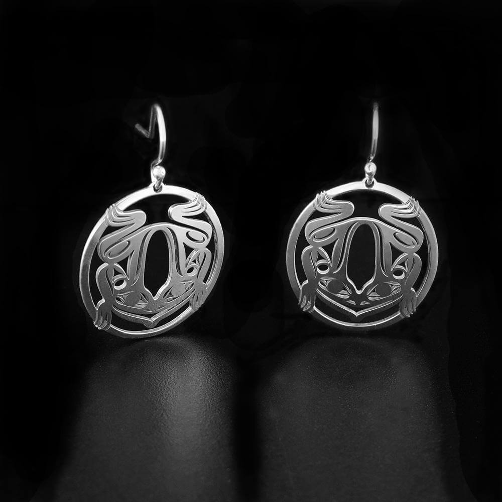 These dangling Frog earrings are made from sterling silver and have circle shaped hangs. There are cutout depictions of the Frog that have been cast into the hangs.