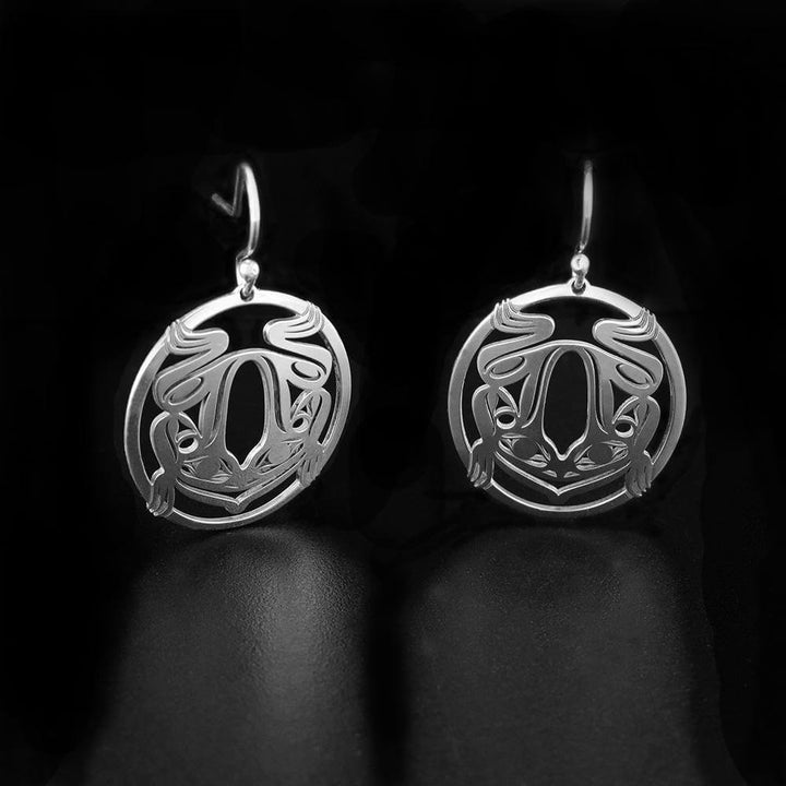 These dangling Frog earrings are made from sterling silver and have circle shaped hangs. There are cutout depictions of the Frog that have been cast into the hangs.