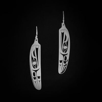 Sterling Silver Raven Feather Earrings by Grant Pauls. Each earring is in the shape of a bird feather. Within each earring the artist has cut out the profile of a raven's head with a sun in its beak facing upward. Following the raven's head, there are intricate designs representing the feathers of the raven.