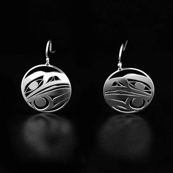 This sterling silver dangle earrings have circle hangs with cutout designs that depict the head of the Raven.