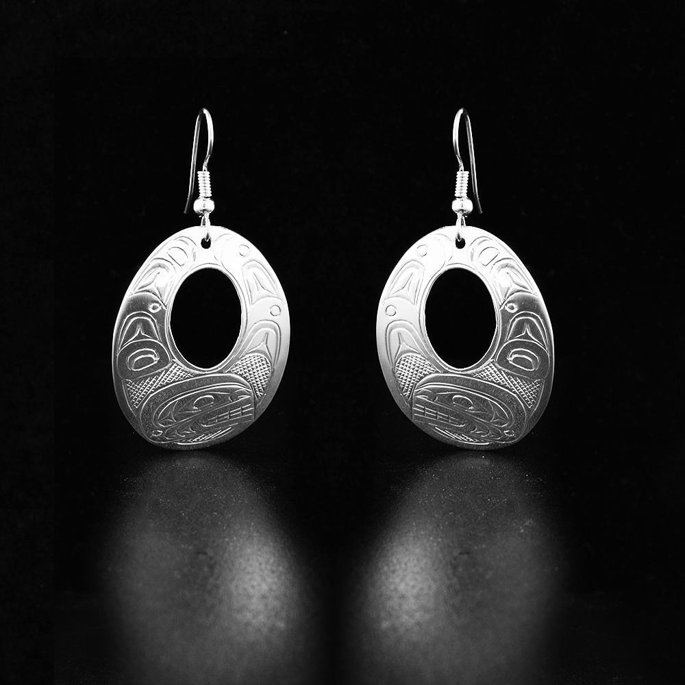 These dangling Orca earrings are made from sterling silver and have oval shaped hangs. There are small, oval shaped cutouts in the center of the hangs and depictions of the Orca carved into the surface of them.