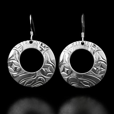 These eagle earrings are circular in shape and have a small cut-out hole in the top center. The bottom of each earring has the profile of an eagle's head with feathers surrounding it.