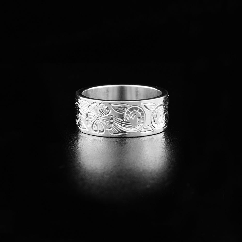 This sterling silver flower ring has a single wide band with carvings on the surface of it depicting plants and flowers.