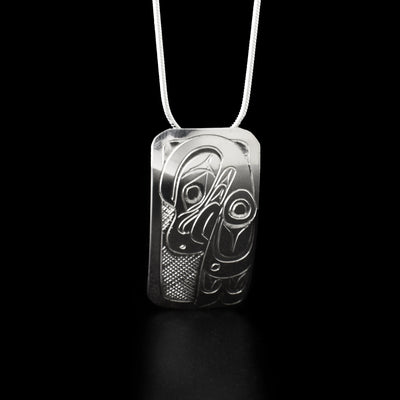 Sterling Silver Rectangular Eagle Pendant by Don Lancaster. The design of the pendant depicts the profile of an eagle's head facing downwards with a short, pointy beak. The artist has also hand-carved a small wing to the right of the eagle's head. Both the head and wing of the eagle have intricate designs hand-carved on them to represents the bird's feathers. The "background" of the pendant has been neatly hand-carved into a crisscross pattern to allow for the legend to stand out.