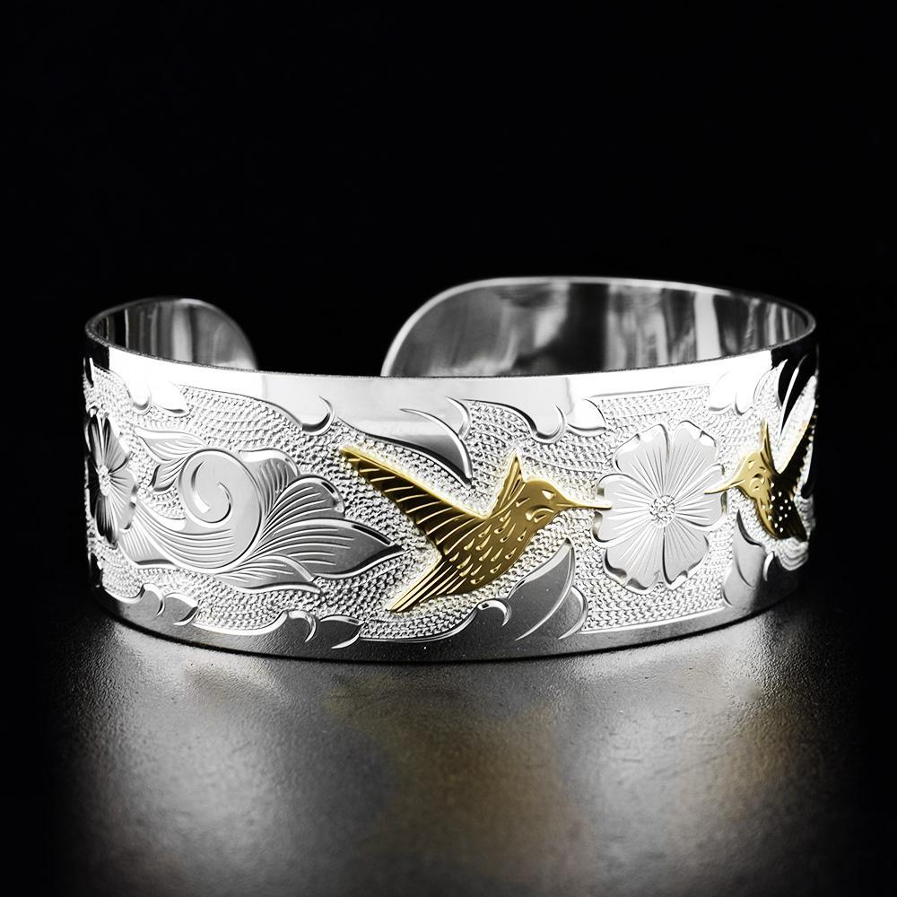 This Hummingbird bracelet cuff has a single, wide band with a gap in the back. There are beautiful depictions of hummingbirds and flowers that have been carved into the surface of the band.