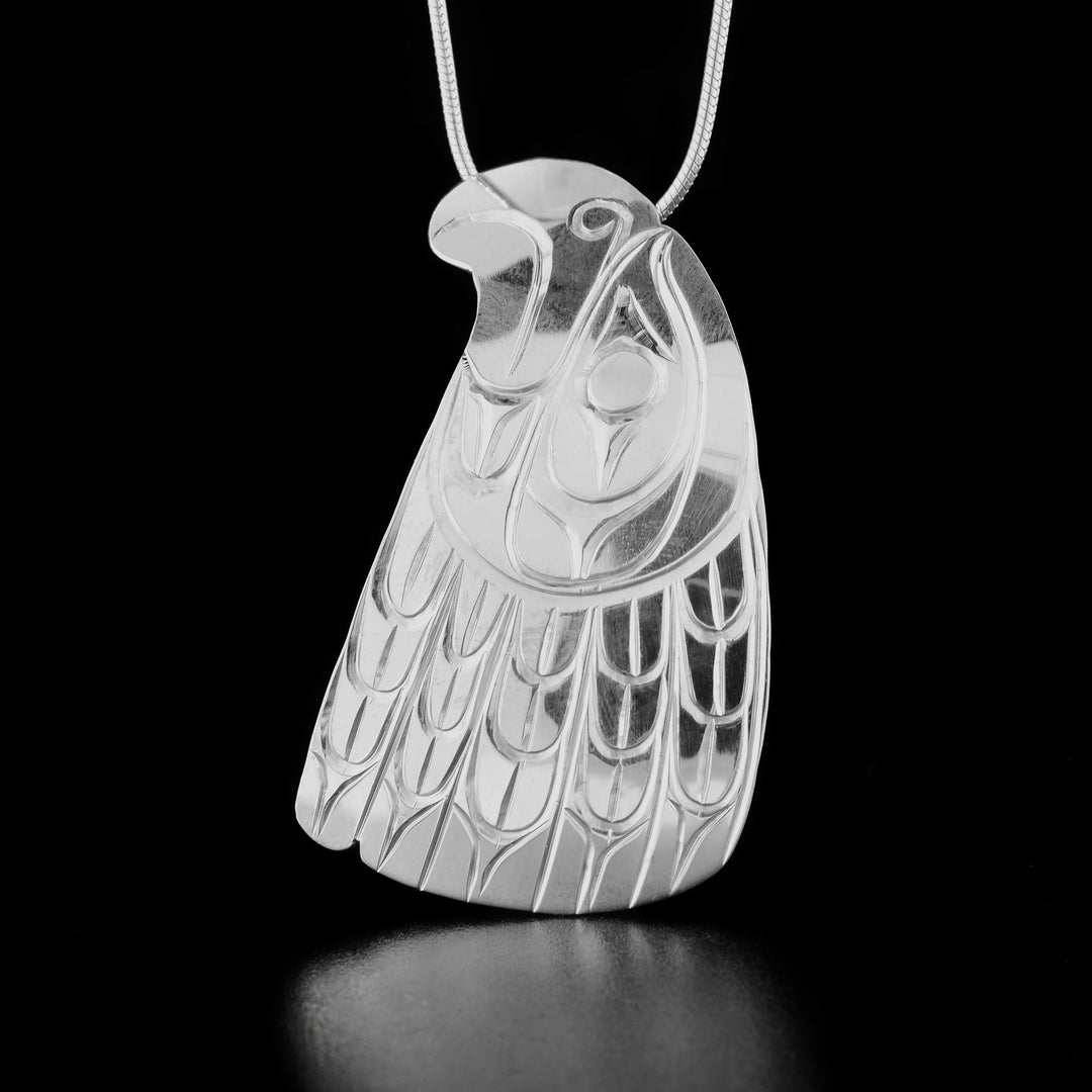 Sterling Silver Head of Eagle pendant by Paddy Seaweed. The pendant is in the shape of an eagle's head. The eagle is looking upward and behind the head are delicately hand carved feathers. The bail is hidden behind.
