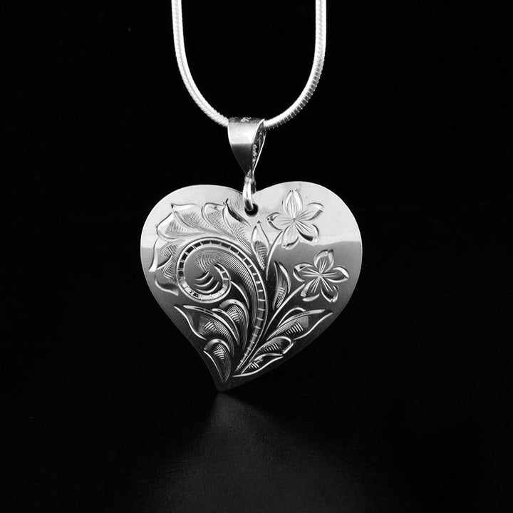 This sterling silver heart pendant necklace has intricate carvings on the surface of it depicting flowers.