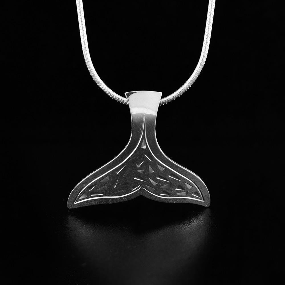 This whale tail pendant is made from sterling silver and is shaped like a whales tail. There are designs carved into the surface of the pendant.