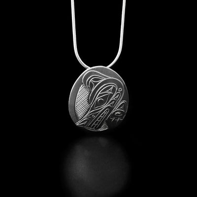 Sterling Silver Oval Wolf Pendant by Don Lancaster. The design on the pendant depicts the profile of a wolf's head looking down to the left corner. The wolf has a long and pointy snout, a pointy ear, and sharp teeth showing. The artist has also hand-carved the wolf's back and paw underneath the its head. The "background" has been neatly hand-carved into a crisscross pattern to allow for the legend to stand out.