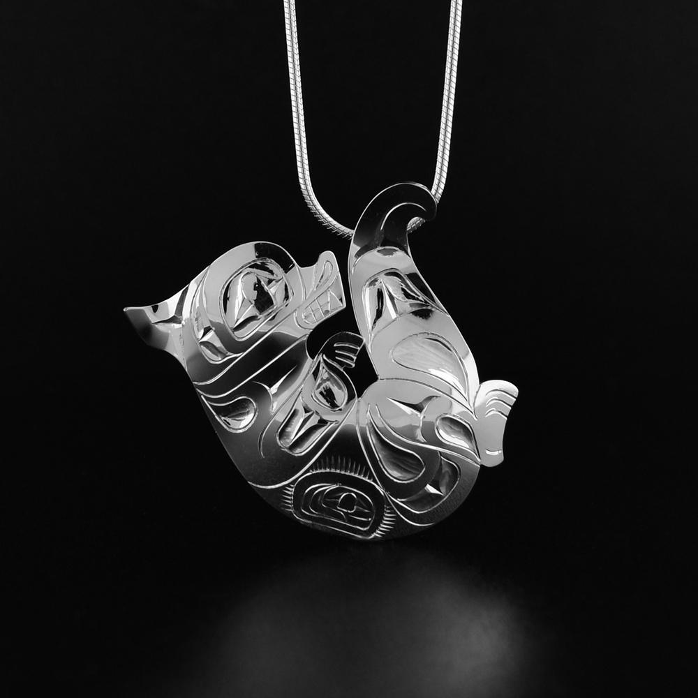 Sterling Silver Otter Pendant by Fred Myra. The pendant is in the shape of an orca laying on its back. The otter has an arm that is reaching up, a leg sticking out, and a tail hat curves upward. The artist has hand-carved intricate designs along the otter's body to represent the fur of the legend.