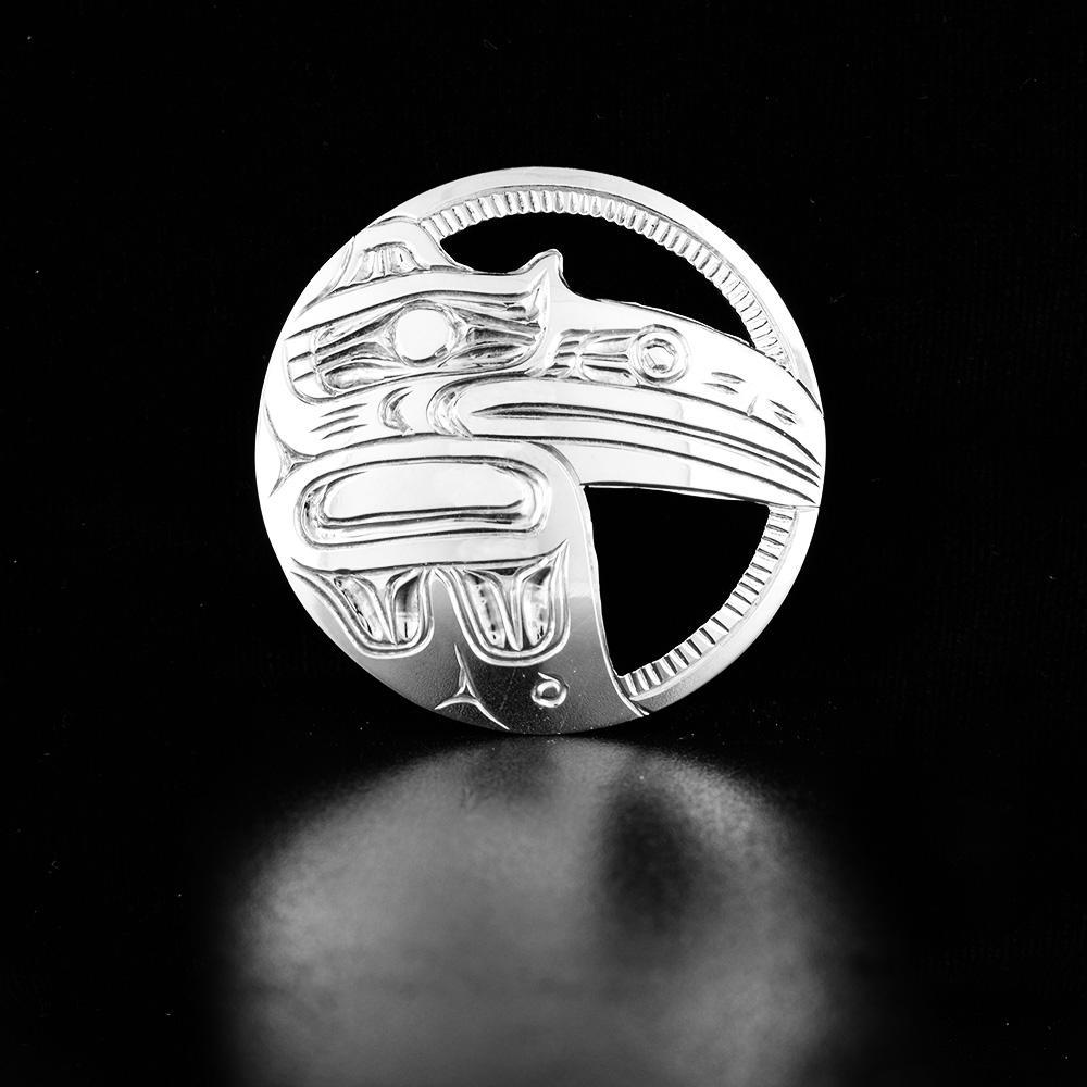 This sterling silver Raven pin is circle shaped and has cutout designs and carvings on the surface of them depicting the Raven.