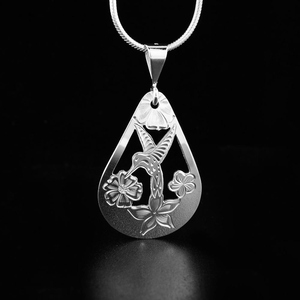 The Hummingbird pendant is made from sterling silver and has a large, teardrop shape to it. There are cutout designs and carvings on the surface of the piece that depict the Hummingbird among flowers.