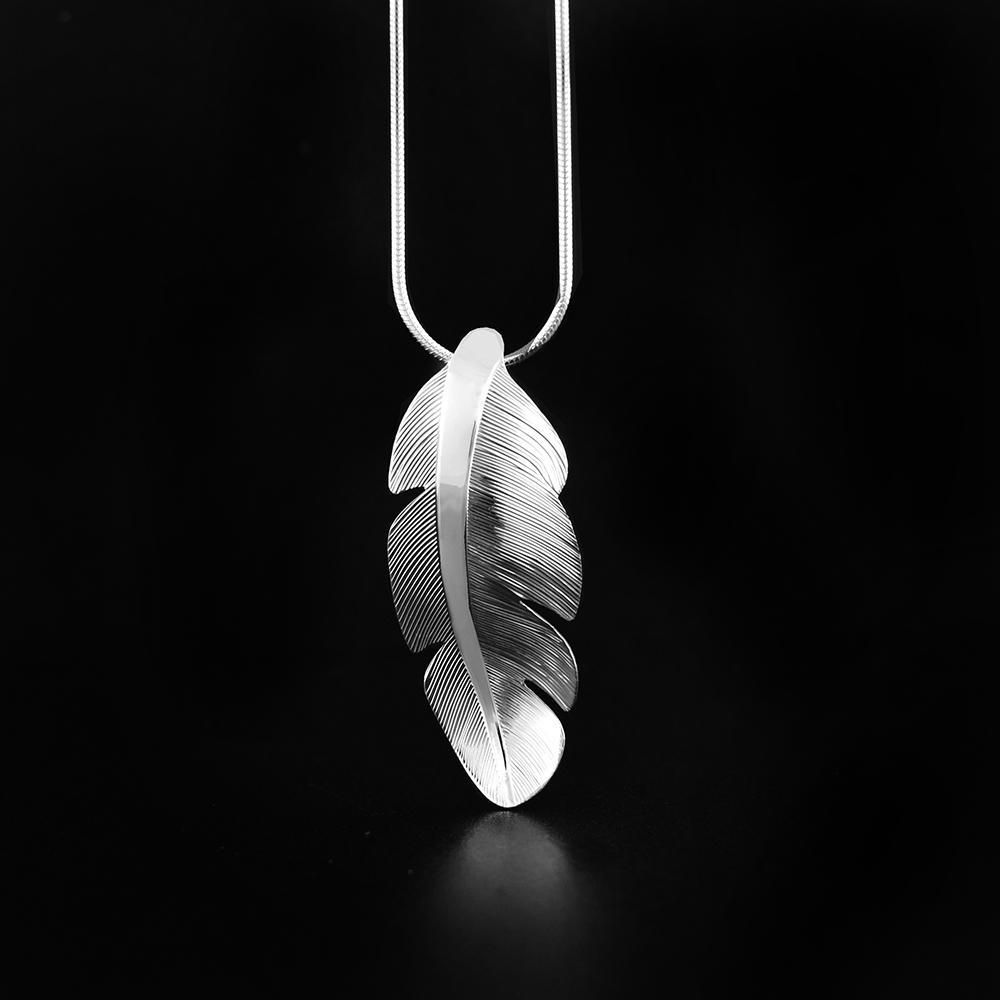 This feather pendant is made from sterling silver and is shaped like and has carvings on the surface of it that depict a feather from the Eagle.