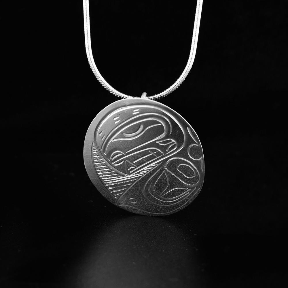 This Orca pendant is made from sterling silver and has a large, oval shape. There is a depiction of the Orca carved into the surface of the pendant.