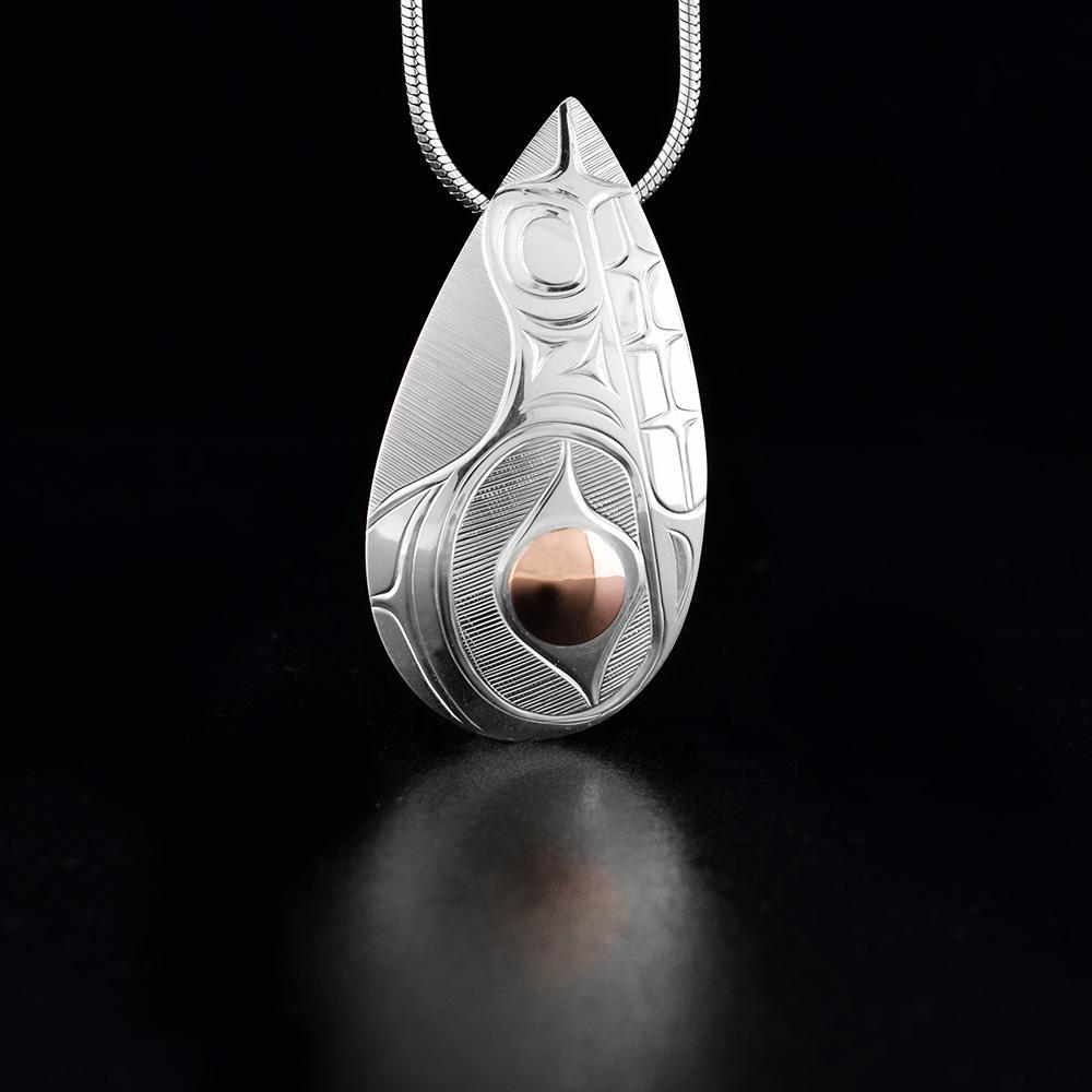 This Bear pendant is made from sterling silver and 18K gold with a large, teardrop shape. There are carvings on the surface of the piece depicting the bear and there is a large, raised gold circle depicting the eye of the legend
