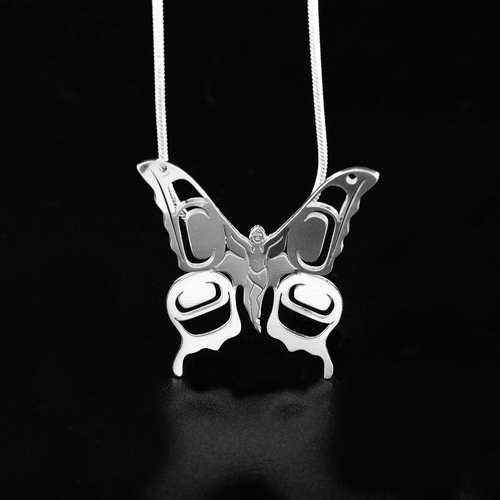 This silver butterfly pendant is made from sterling silver and is shaped like a butterfly. There are cutout designs on the wings and the body of the butterfly has carvings that depict a small person.
