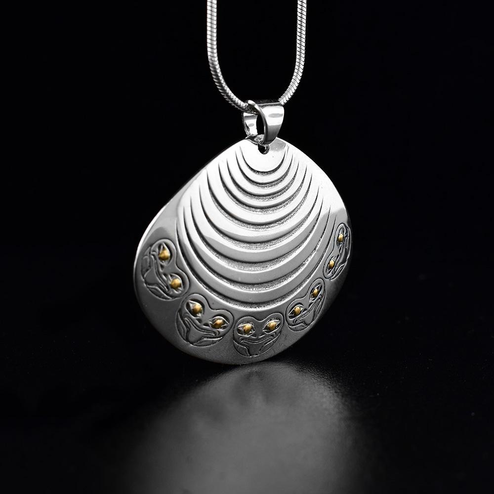 Sterling silver and 18K gold Clam and Frog pendant. Design depicts a clam with frogs decorating the bottom. Eyes of the frogs are made from 18K gold and rest of piece is sterling silver. Measures 1.25" x 1.50". Chain not included.