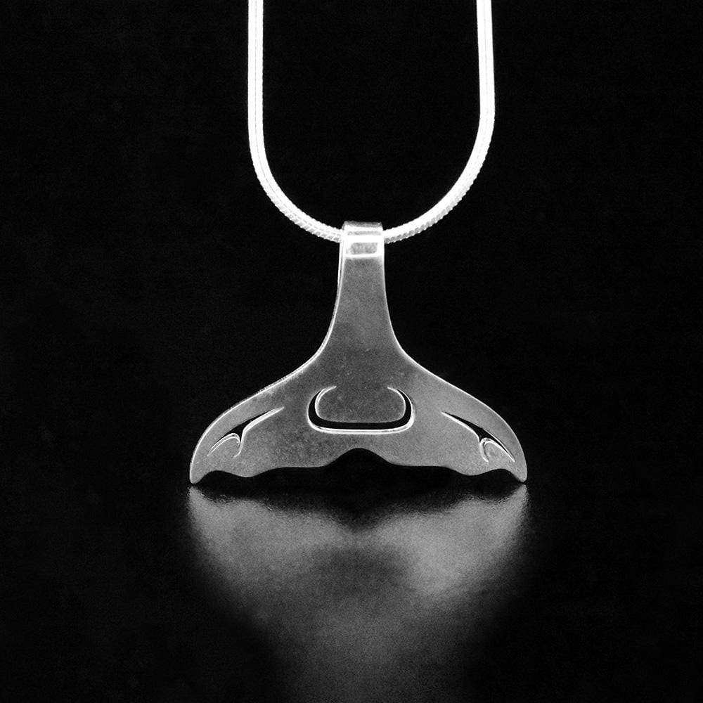 This whale tail pendant is made from sterling silver and is shaped like a whale tail. The piece features cutout designs that have been made on the surface of it.