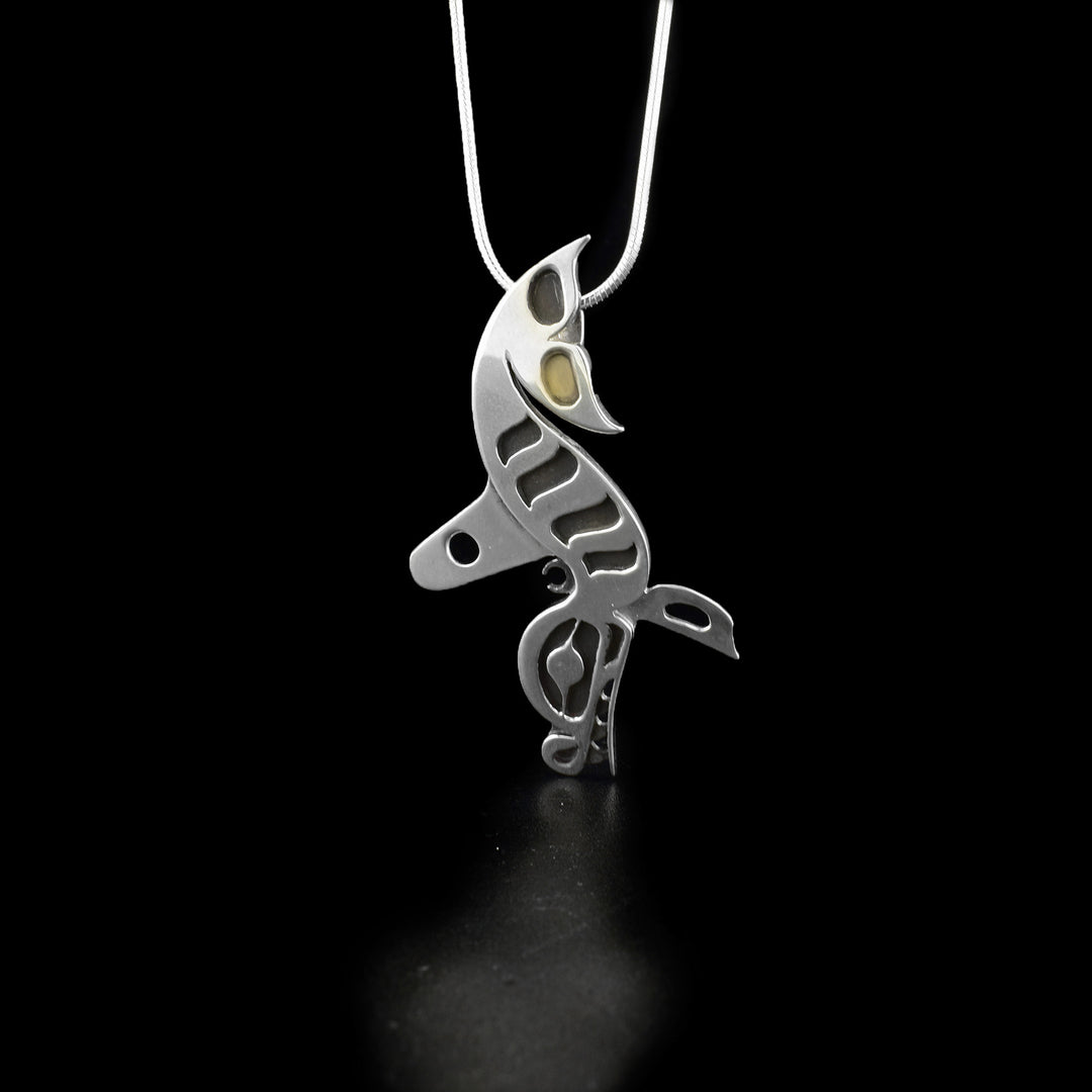 This orca pendant is in the shape of a full-body orca facing downwards. The layer underneath has been oxidized and can be seen in the carvings of the orca's body.