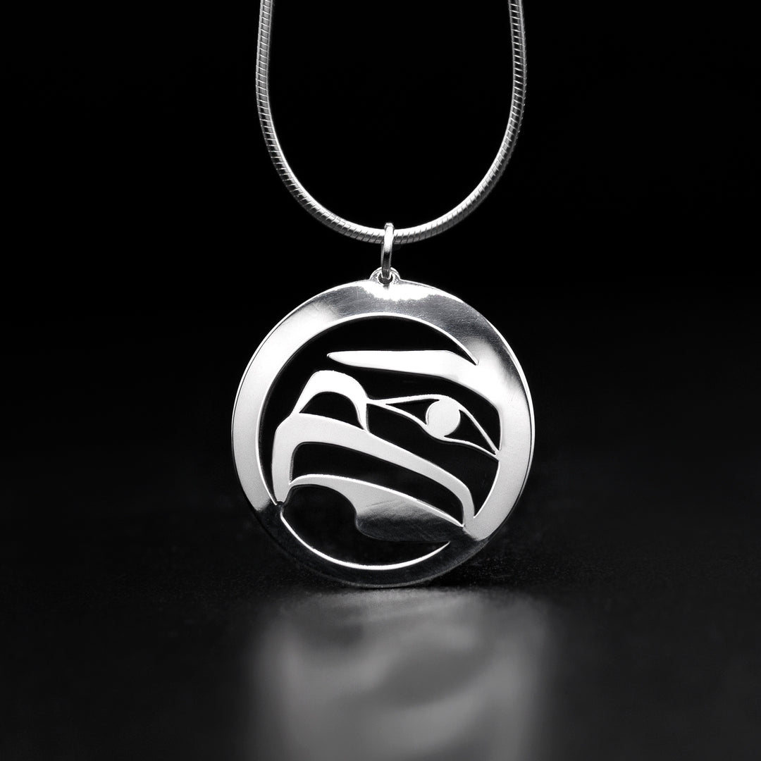 This Eagle pendant is round in shape and depicts the sideview of an eagle's head facing the left. The background of the pendant and parts of the eagle have been cut out to give it depth.