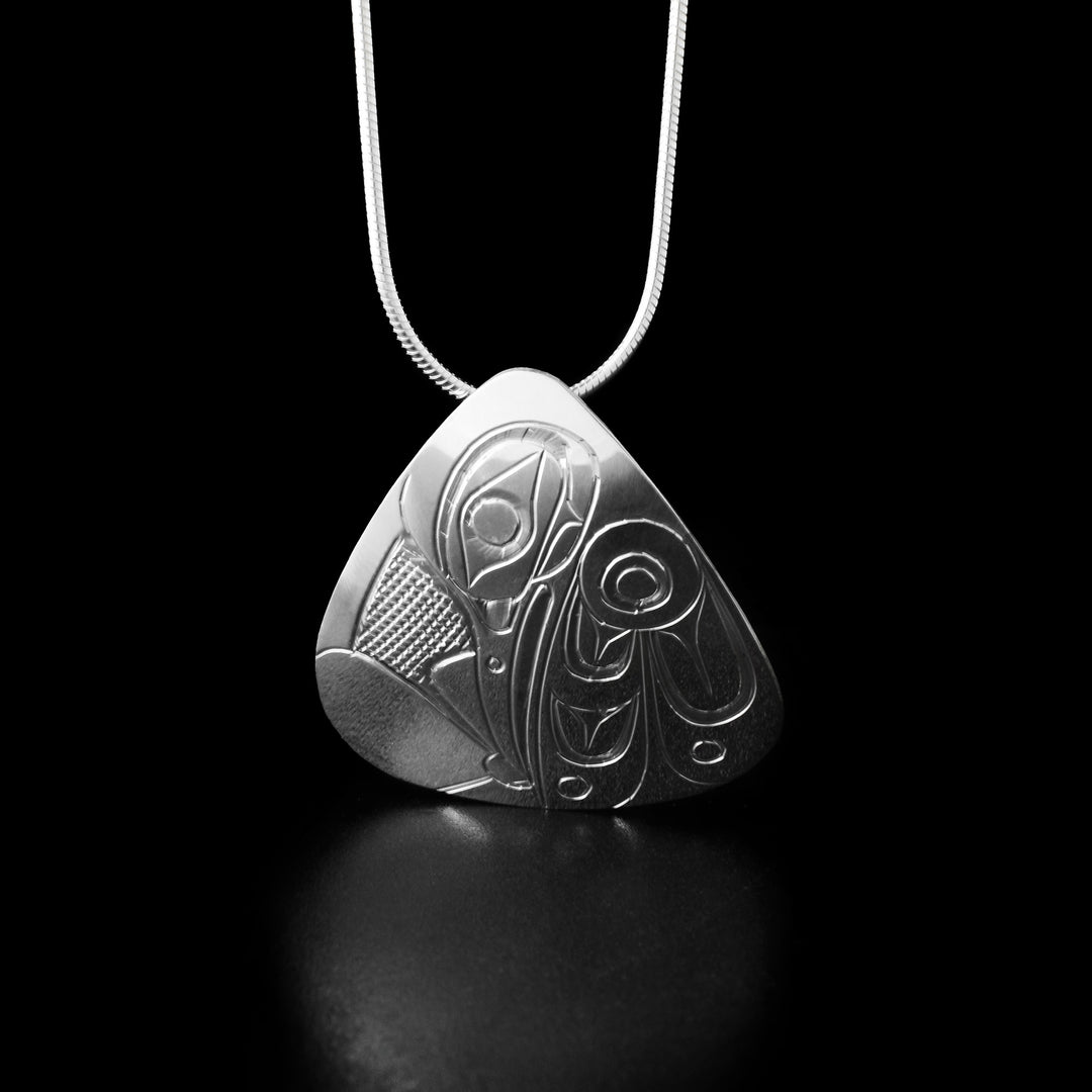 Sterling Silver Triangle Hummingbird Pendant by Don Lancaster. The design depicts the profile of a hummingbird's head facing downwards and drinking from a flower which the artist has hand-carved at the bottom of the pendant. To the right of the hummingbird's head is its wing with intricate designs representing its feathers. The "background" has been hand-carved into a crisscross pattern to allow for the legend to stand out.