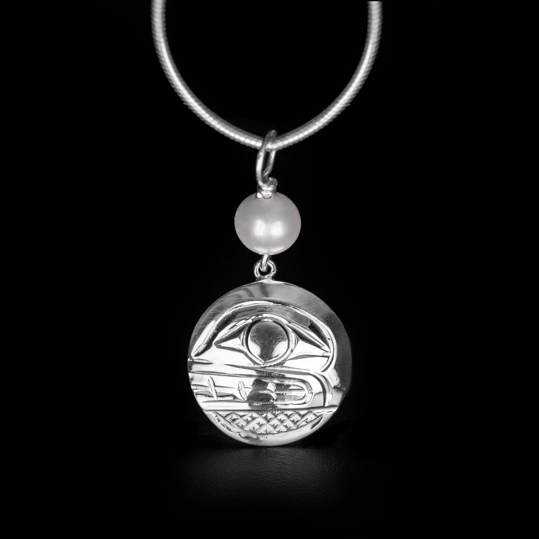 This unique Orca pendant is made from sterling silver and a large, freshwater pearl. The pendant is circle shaped and made from silver; there is a depictions of the Orca carved into the pendant. The spherical pearl bead is strung above the pendant.