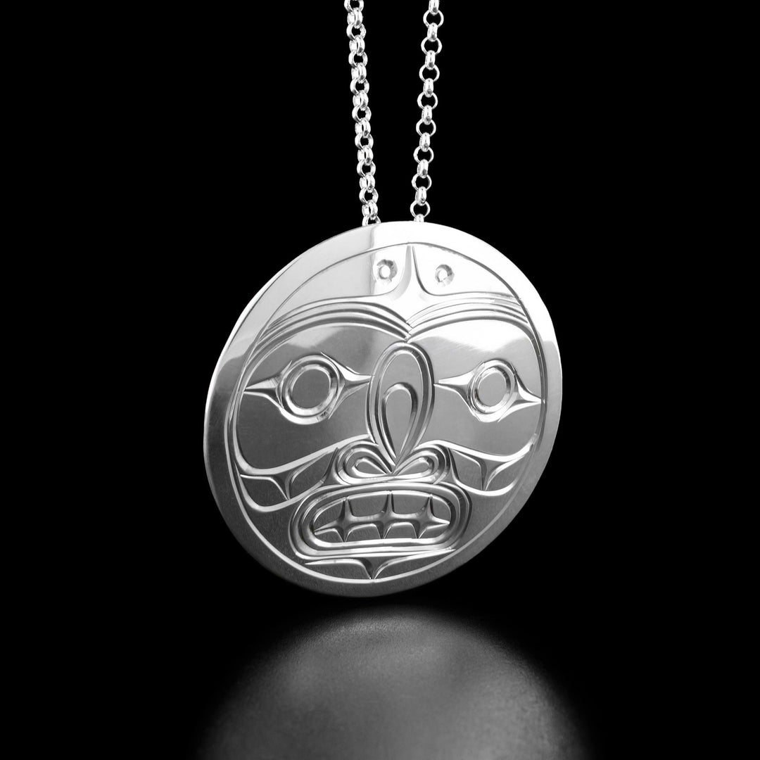This silver moon pendant has the face of the moon in the center looking forward. The moon has a large nose and an open mouth with teeth.