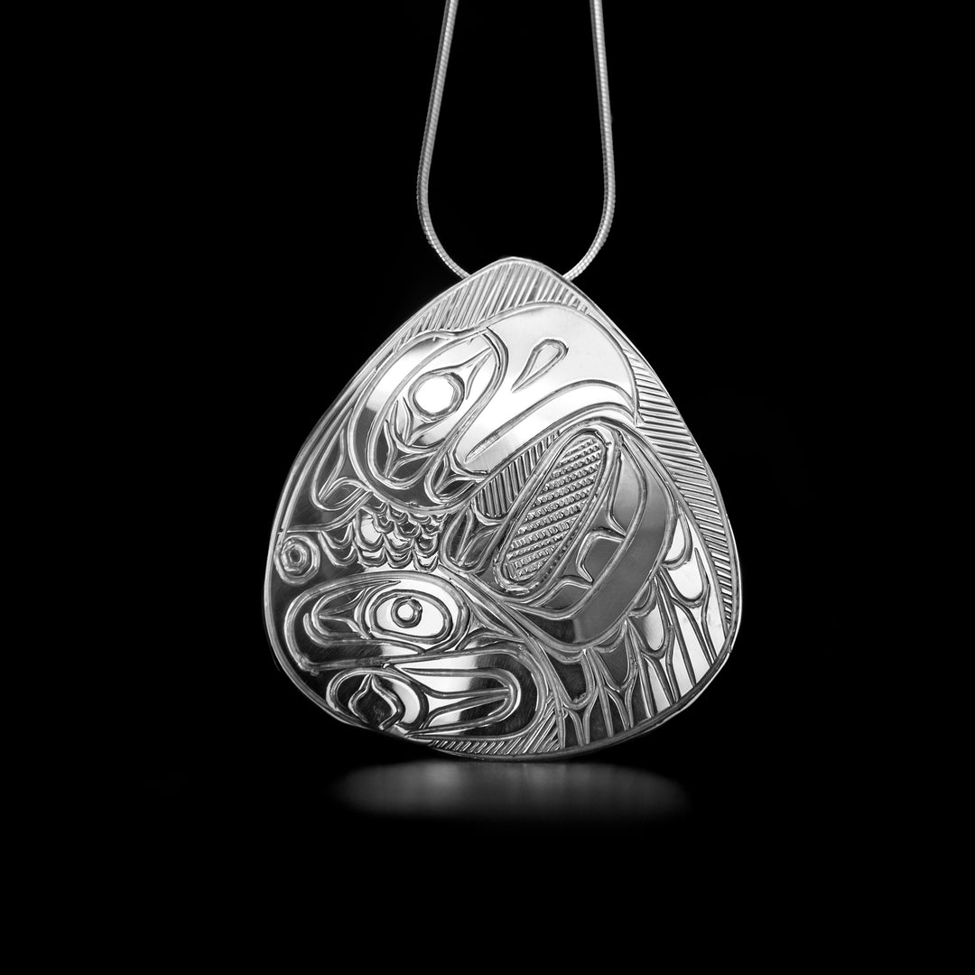 Sterling Silver Thunderbird Pendant by Paddy Seaweed. The design depicts the profile of a thunderbird's head facing to the right with a large, spread out wing underneath the head. The body and neck of the thunderbird has been filled with intricate designs. The artist has hand carved delicate feathers into the spread out wing of the bird.