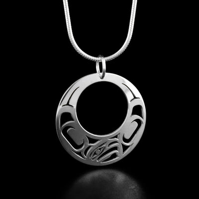 Sterling Silver Mini Offset Eagle Pendant by Grant Pauls. The pendant is a circular shape with a large hole in the center. There is a profile of an eagle's head facing the right at the bottom with intricate designs on both side of the animal.