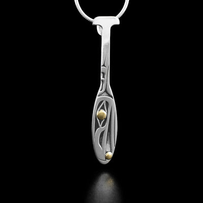 Sterling Silver and 18K Gold Raven Paddle Pendant by Grant Pauls. The design depicts the profile of a raven's head facing downward with 18K gold in the eye and in the raven's mouth.  The background is oxidized sterling silver.