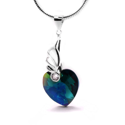 Emerald Swarovski Crystal Heart Pendant by Debra Nelson. The green Swarovski crystal has been cut into a heart shape. The artist has handcrafted an intricate bail and has attached it to the top of the heart-shaped crystal. She has then set a cubic zirconia at the bottom of the bail. The Swarovski crystal has hues of green, blue, and orange.