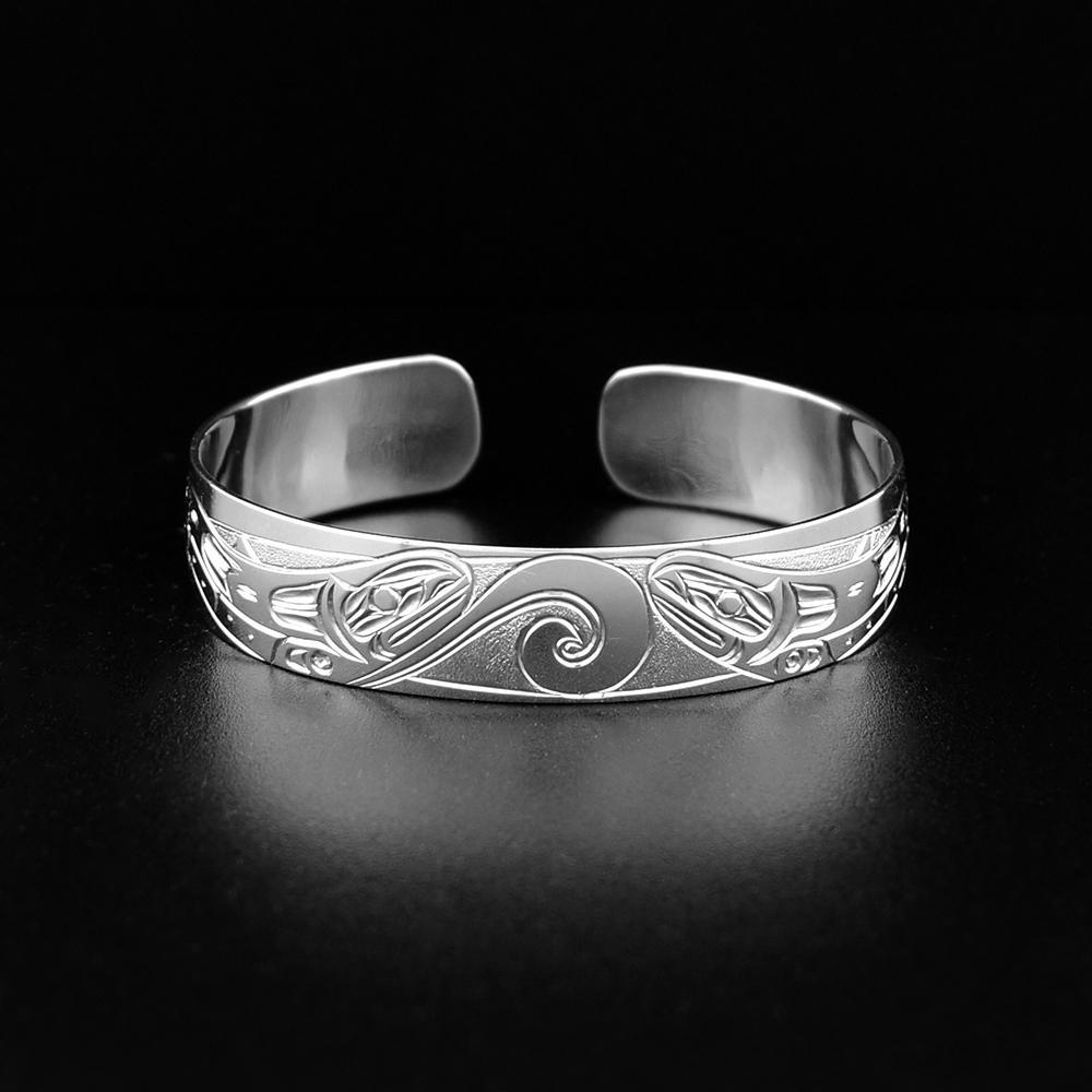This Salmon bracelet cuff is made from sterling silver and has a single band. There are two depictions of the Salmon facing each other carved into the surface of the band.