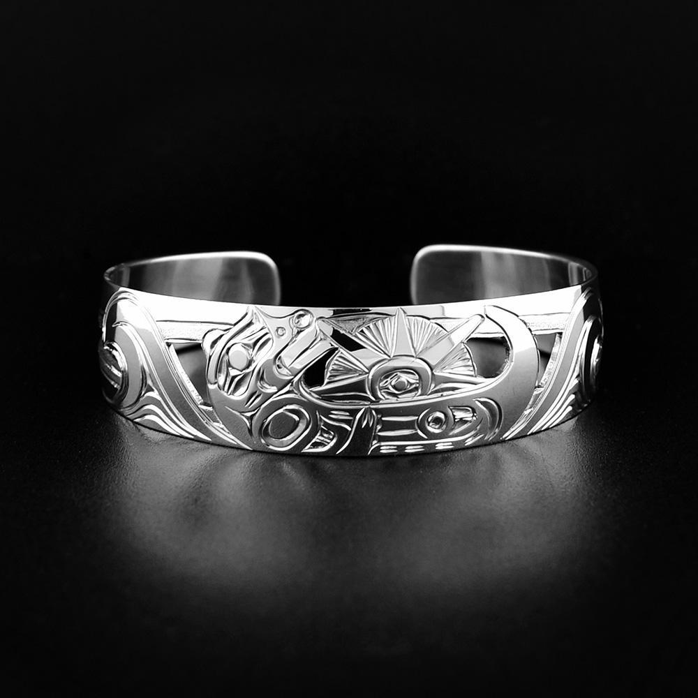 This Otter bracelet is made from sterling silver and has a single, wide band with a gap in the back. There is a depiction of the Otter laying on its back holding a sea urchin in the ocean.