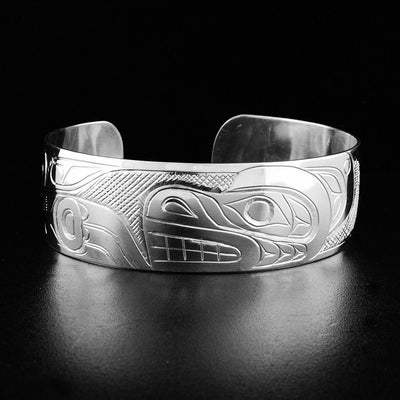 This silver cuff bracelet depicts the head of a bear facing the left in the center. To the left is its paw and body. Background is cross-hatched.