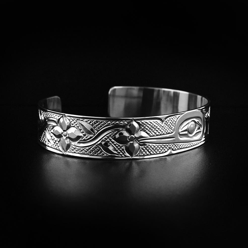 This Hummingbird bracelet is made from sterling silver and has a single band with a gap in the back. There is a depiction of the Hummingbird among flowers carved into the surface of the band.