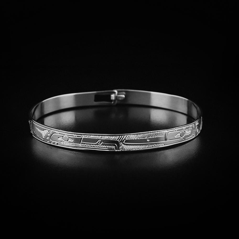 This sterling silver bangle bracelet has a thin band and a clasp in the back. There are depictions of the Eagle and the Hummingbird carved into the surface of the band.