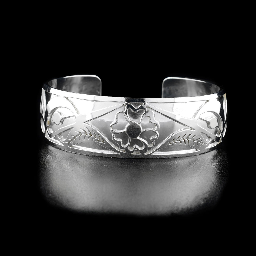 The center of this hummingbird bracelet has a flower with two leaves. On both sides of the flower are the heads of two hummingbirds facing inward and drinking from the flower.