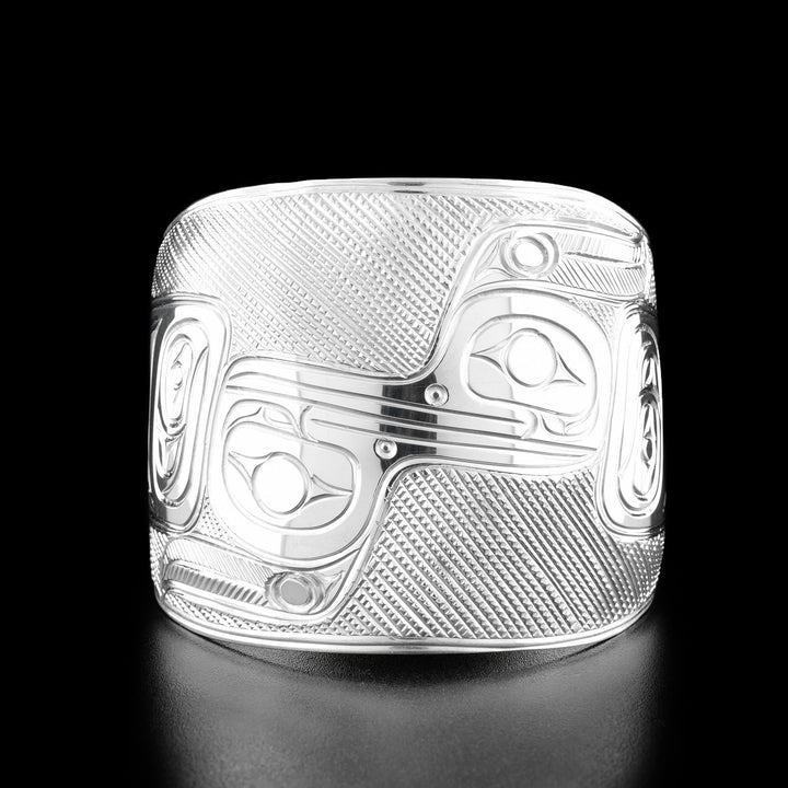 Sterling Silver Hummingbird Reflection Bracelet by Paddy Seaweed. The design depicts one hummingbird on the right side of the bracelet looking to the left. The second hummingbird is upside down on the left side of the bracelet looking to the right. The beaks are connected to make it appear as if the two hummingbirds were being reflected. The background has been carefully designed to allow for the image to stand out.
