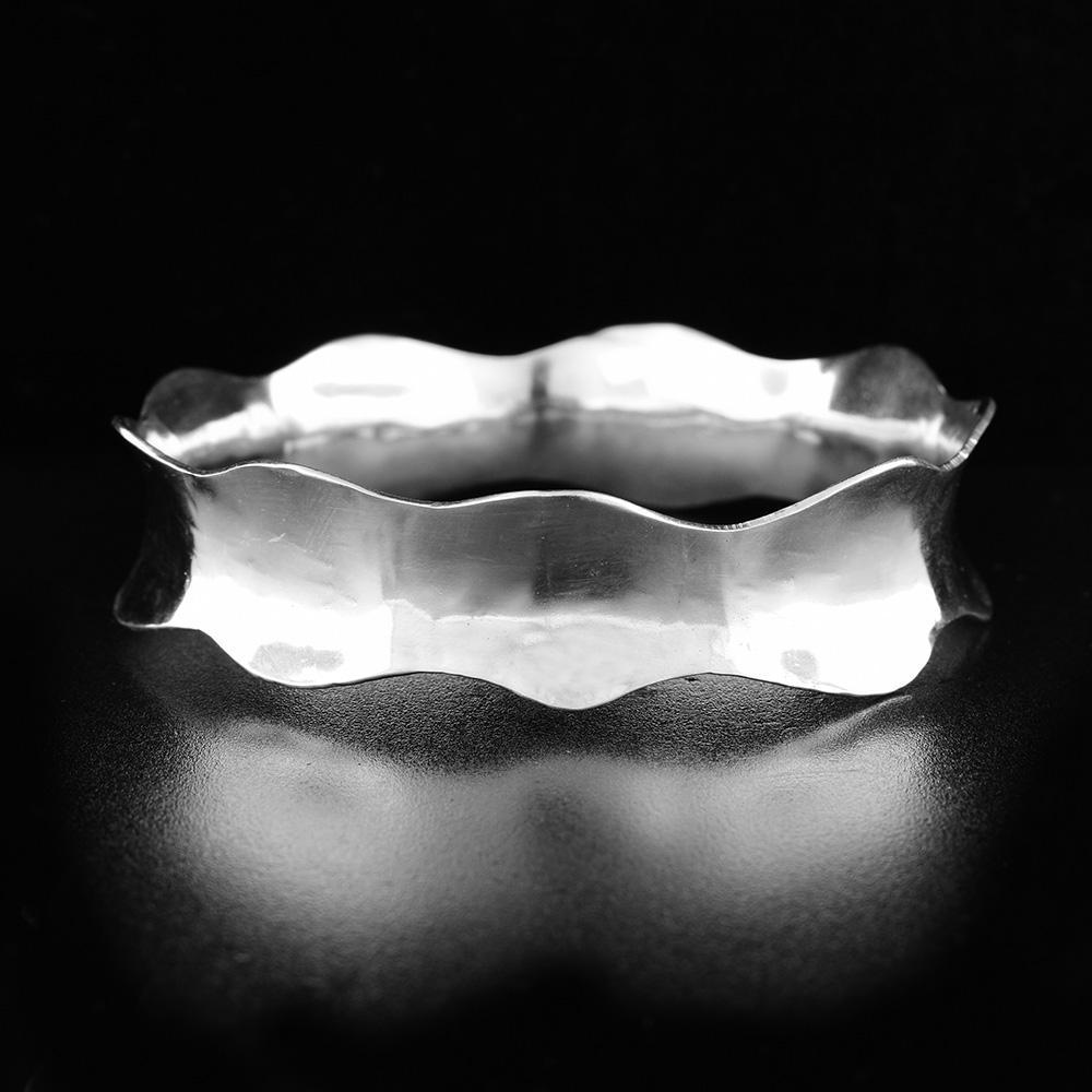 This wavy bangle bracelet is made from sterling silver and has a concave band that wraps all the way around the wrist. The band has a wavy shape around the whole bracelet.
