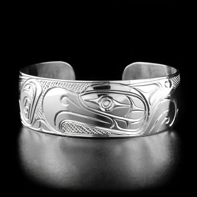 Sterling Silver 3/4" Thunderbird Bracelet by Paddy Seaweed. The design depicts the profile of a thunderbird's head facing the left in the center of the bracelet. The right depicts the continuation of the thunderbird's body and displays a large, spread out wing. The background has been neatly hand carved in a cross-hatch pattern to allow for the thunderbird to stand out.