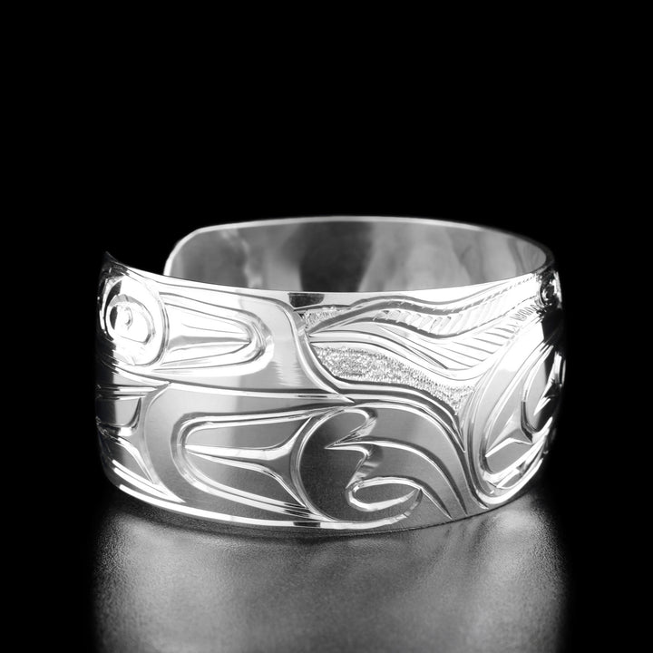 Left angle photo of the bracelet shows carved designs representing the raven's body as well as its spread out wing as if mid-flight.