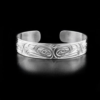 Sterling Silver 1/2" Eagle and Orca Bracelet by Paddy Seaweed. The design depicts the profile of two eagle heads facing away from each other in the center of the bracelet. On both sides are the profiles of two orca heads facing towards the center of the bracelet followed by intricate designs at the very end. The background has been delicately hand carved to allow for the image of the legends to stand out.