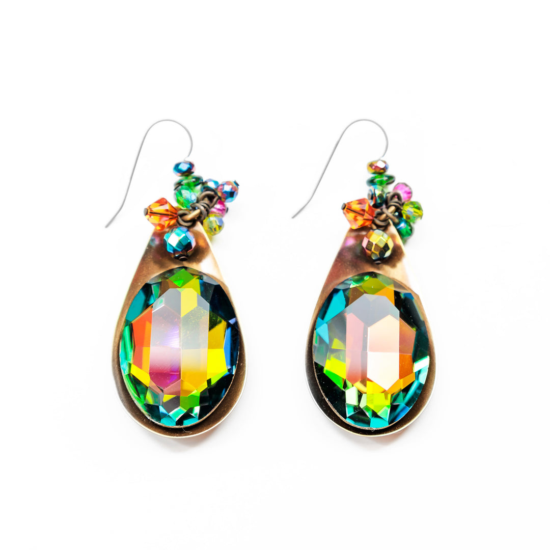 These colorful crystal earrings have been made using oval shaped Swarovski crystal, hand worked brass, and an array of beautifully cut and colorful glass beads. The oval shaped crystal has been backed on a teardrop shaped brass piece and there is a cluster of glass beads below the hooks.