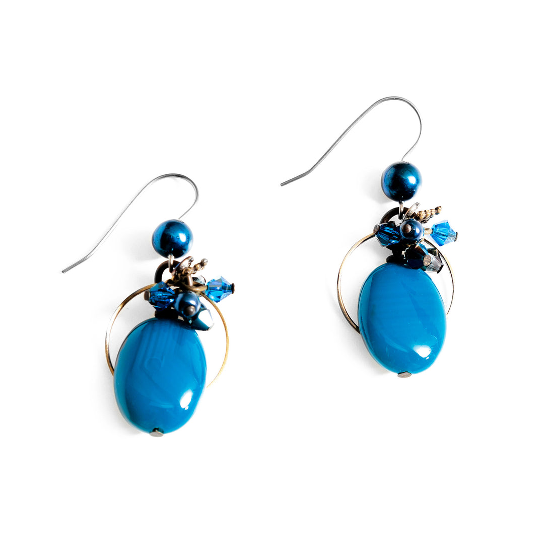 These unique blue agate earrings have been made using hand worked brass, freshwater pearls, Austrian crystal, and dyed agate. There is a cluster of small beads below the hooks made from Austrian crystals and pearls. Below the cluster are large teardrop shaped blue agate gems. There are black pearls that run through the hooks above the rest of the piece.